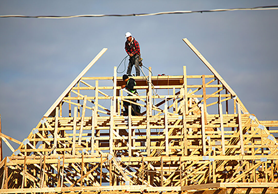 Vaughan, Ontario, Canada - October 14, 2016: Two roofers standing on top of the new roof frame for a new house. Construction site of new detached houses being built in Vaughan - Major MacKenzie Drive West and Via Romano Blvd (Patterson Community)